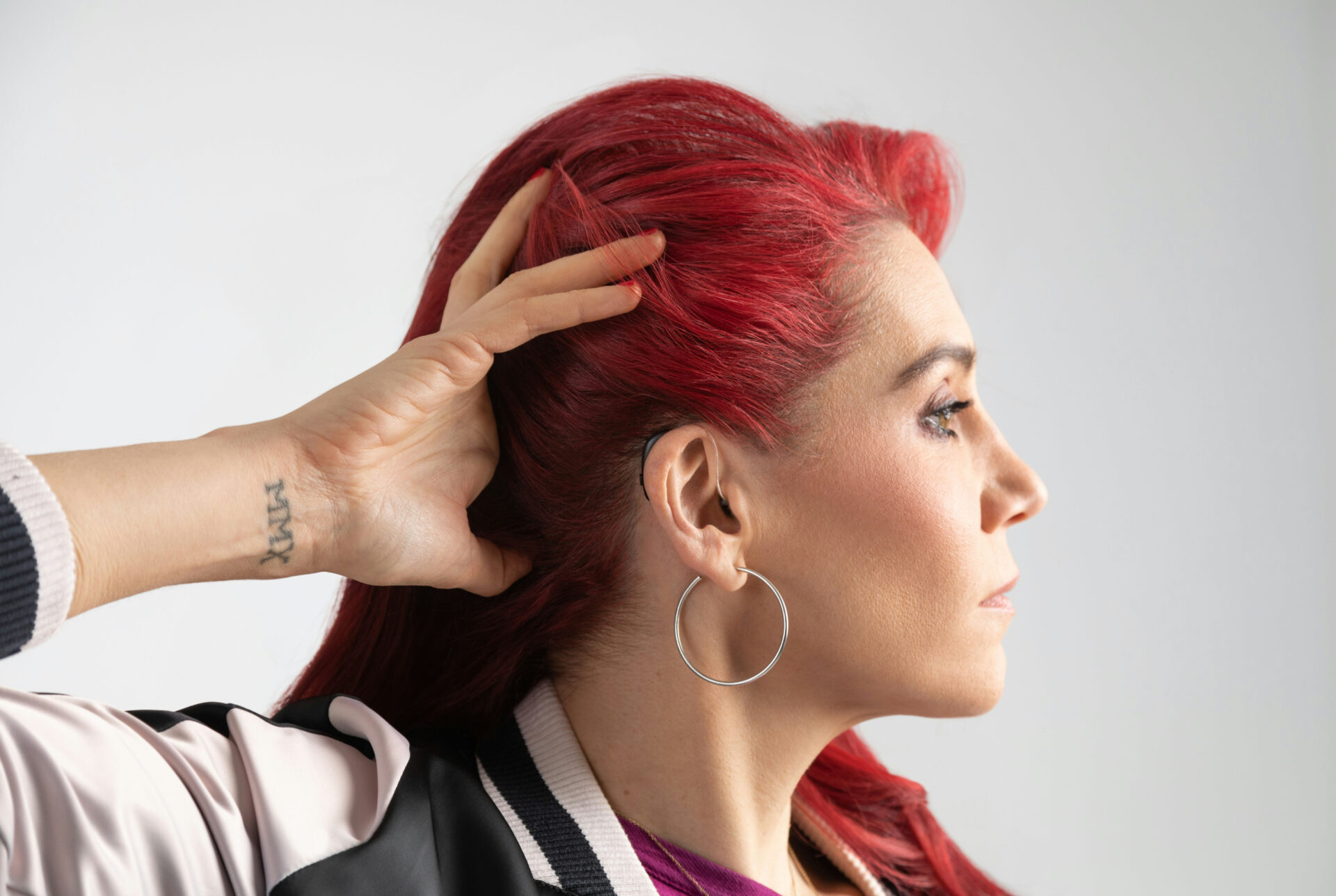 Woman with red hair wearing a receiver-in-the-canal hearing aid. Holding hair up to show hearing aid.