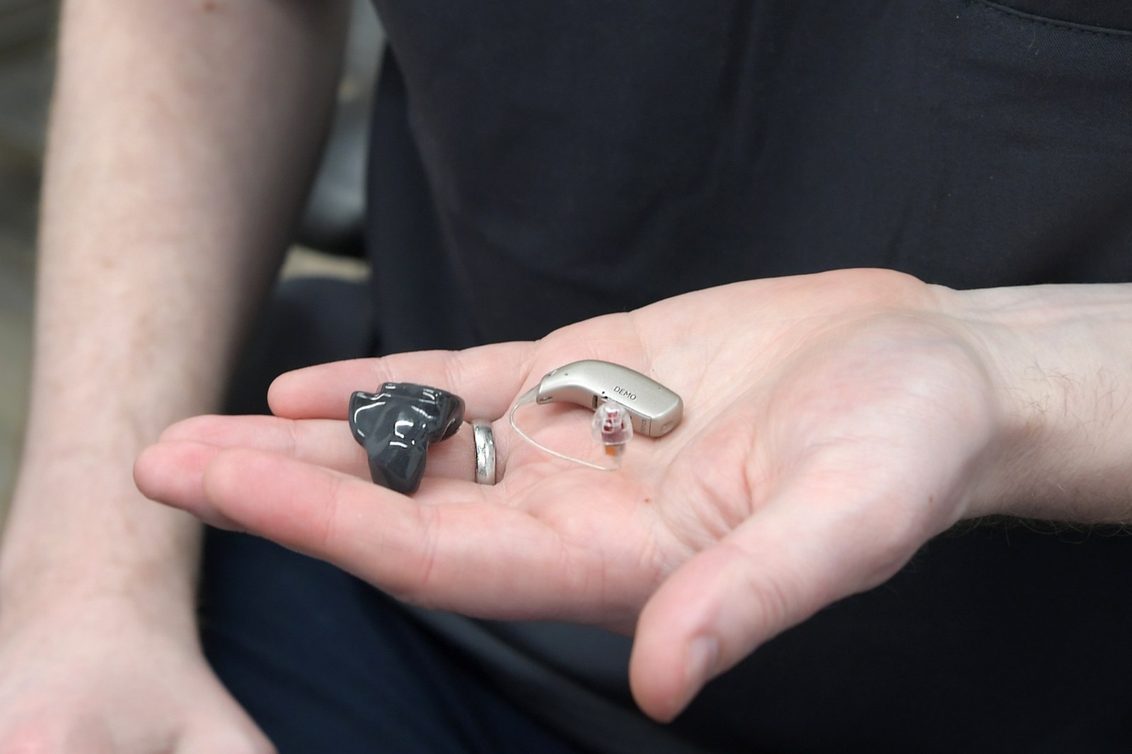 A custom in-ear hearing aid on the left and a receiver-in-the-canal hearing aid on the right, side by side in a clinician’s hand