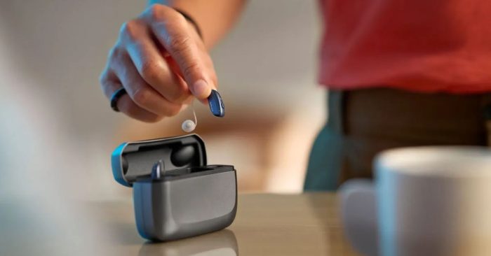 Best Hearing Aids - Resound Vivia hearing aids in portable charger on desk, with one hearing aid being lifted out