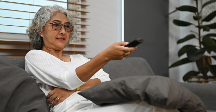 Where could Auracast be used? Woman watching TV holding remote control