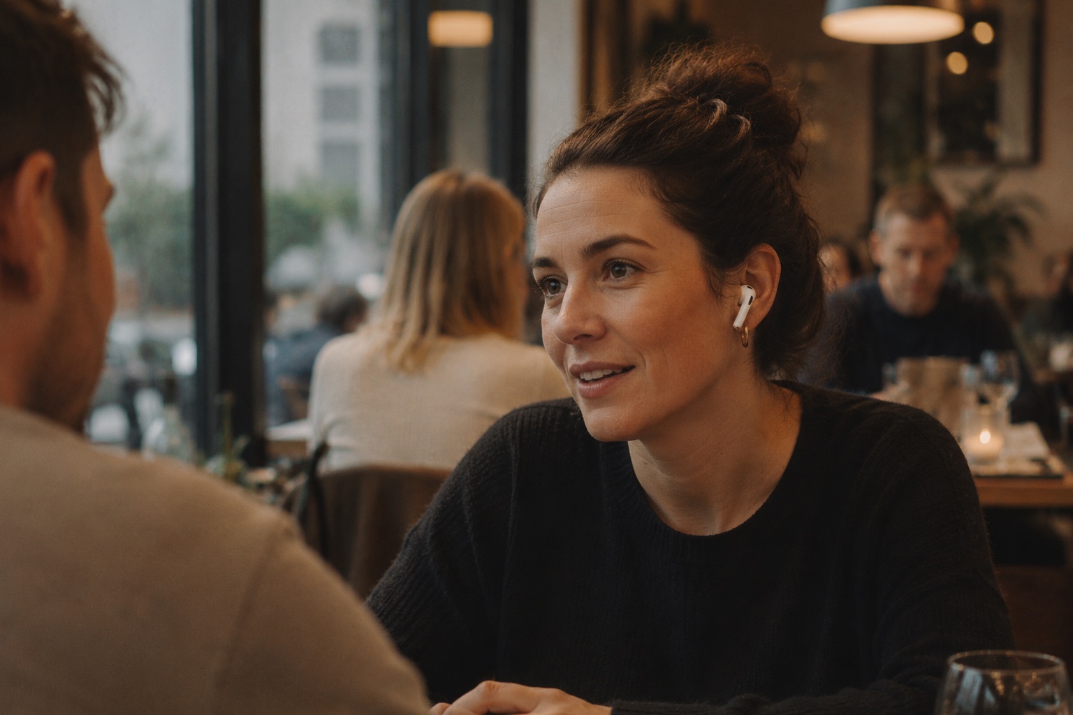 Person using AirPods hearing features during conversation in a restaurant