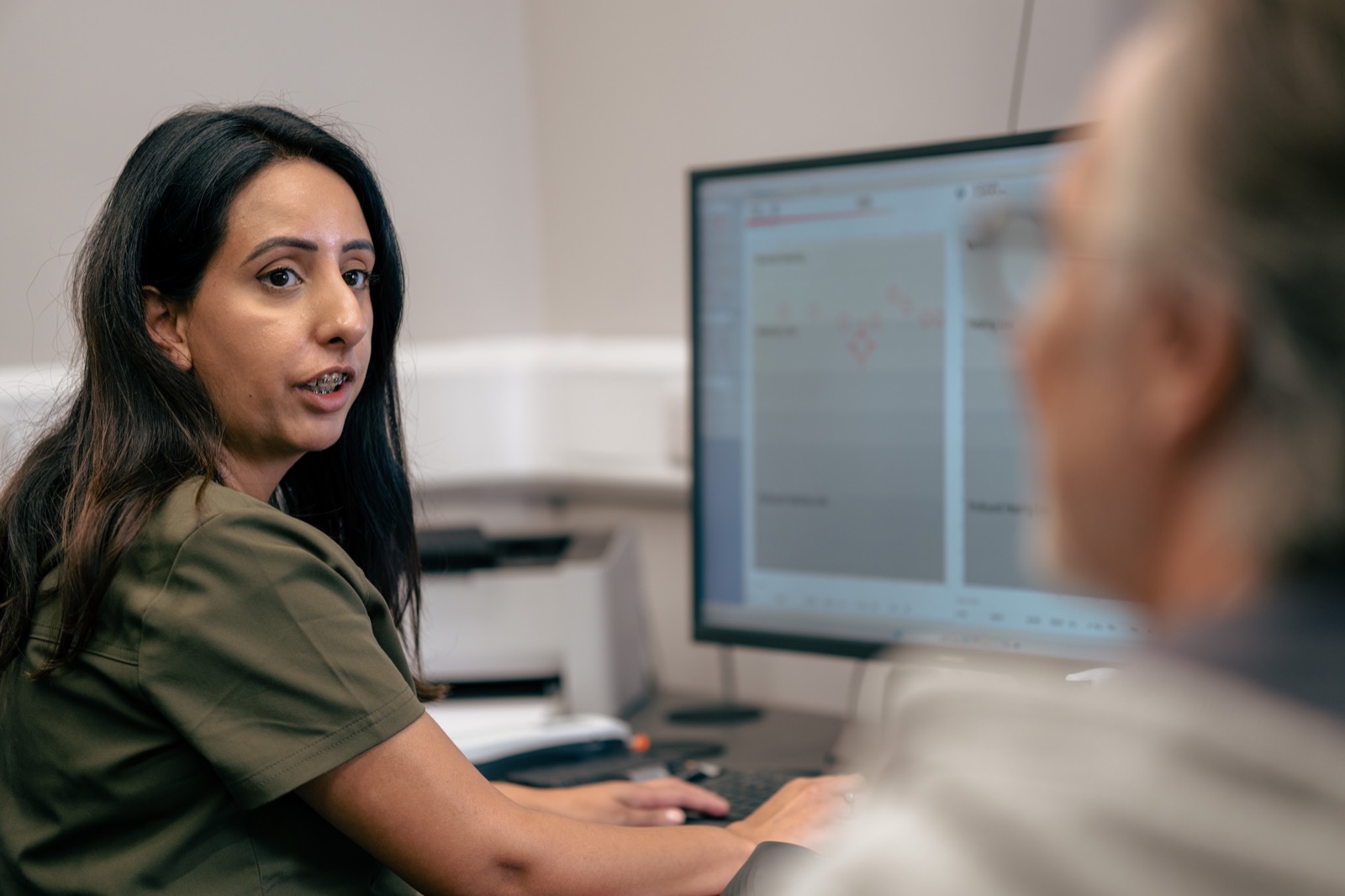 An Alto clinician discussing hearing care with a client beside a computer screen