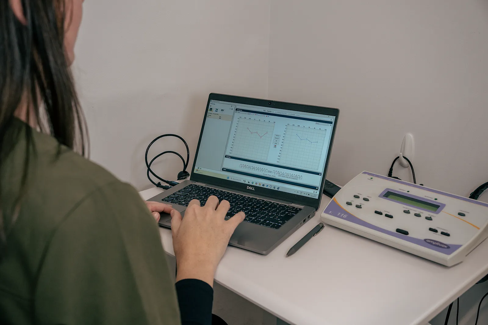 Alto clinician using a laptop and audiometer during hearing testing