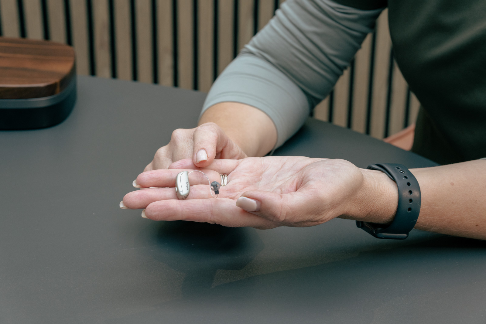 Receiver-in-canal hearing aid with a silicone dome resting in an open hand.