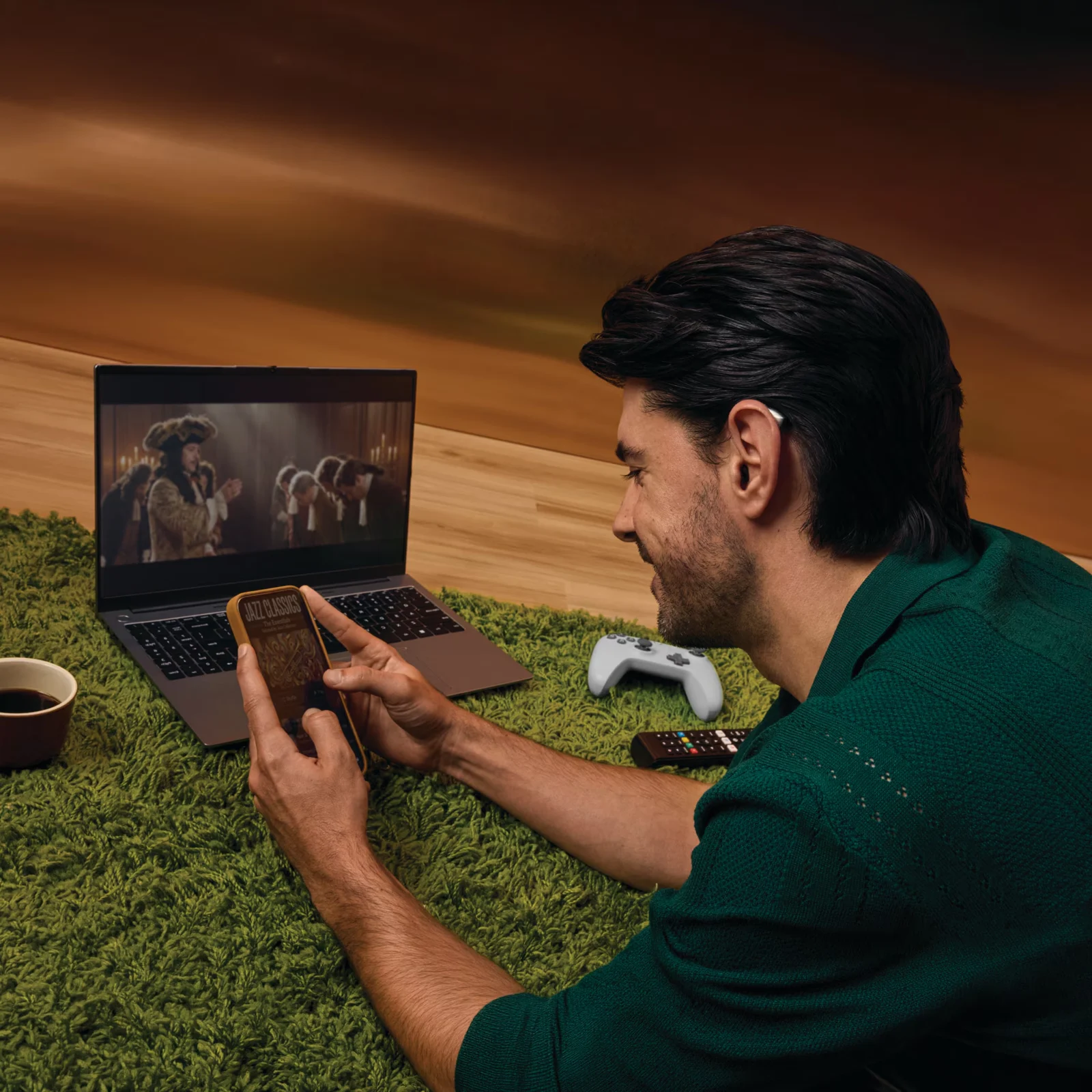 Hearing-aid wearer using a smartphone beside a laptop playing a video