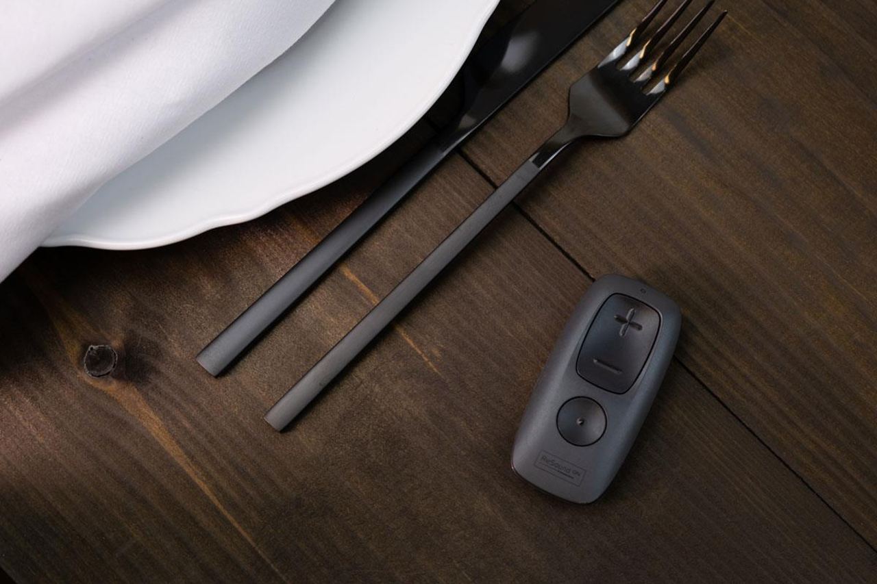 ReSound Remote Control on a dining table, showing its large plus and minus volume buttons
